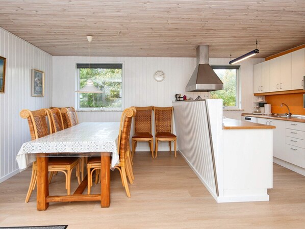 A compact kitchen with a central island, a dining area with wooden chairs, and a large window providing natural light.