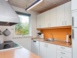 A modern kitchen with white cabinets, a wooden countertop, a built-in dishwasher, and a window with a view of trees. - 8 Person Holiday Home in Ulfborg (Ulfborg)