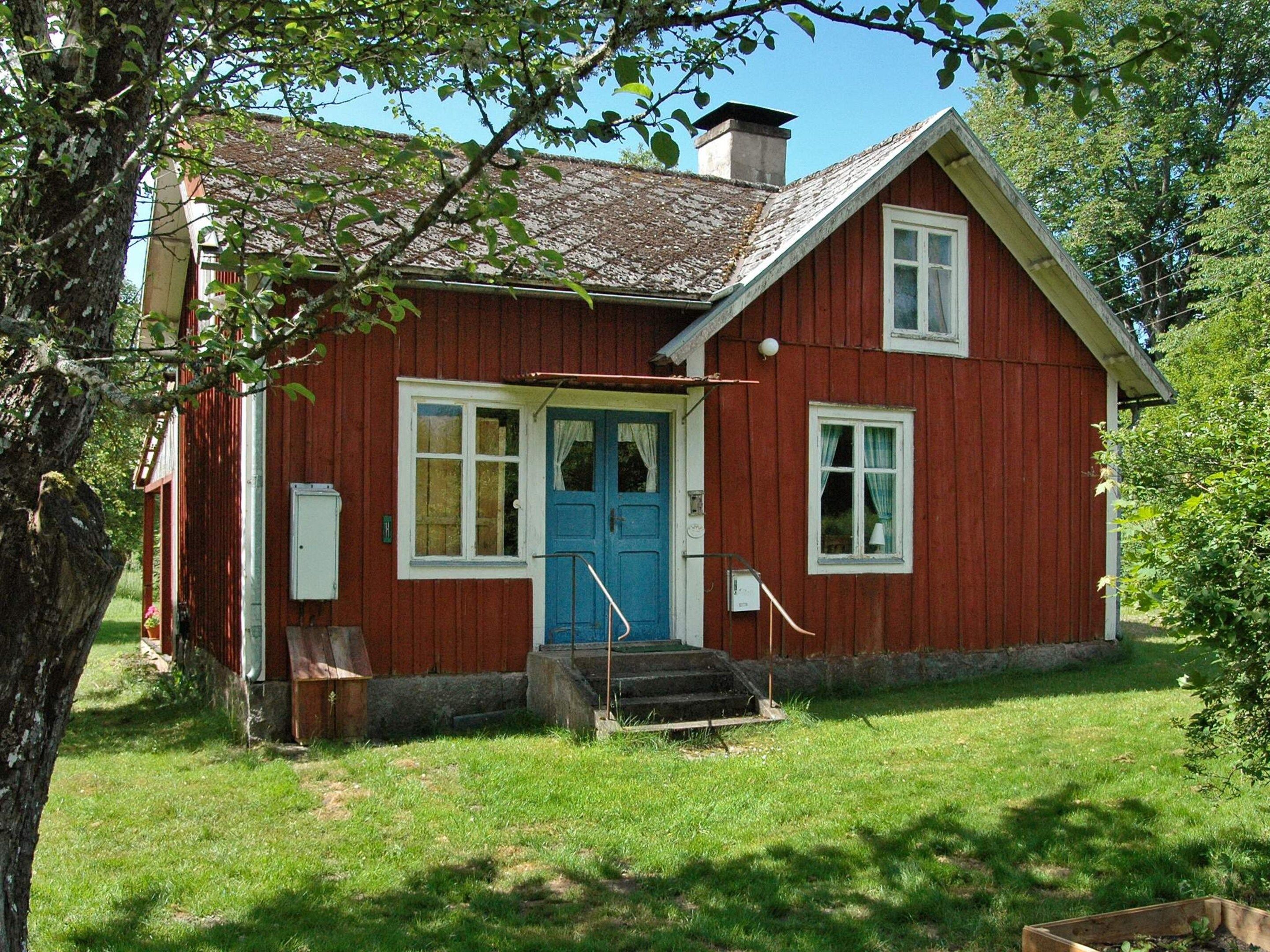 A red wooden house with a blue door, white windows, and a small porch.
