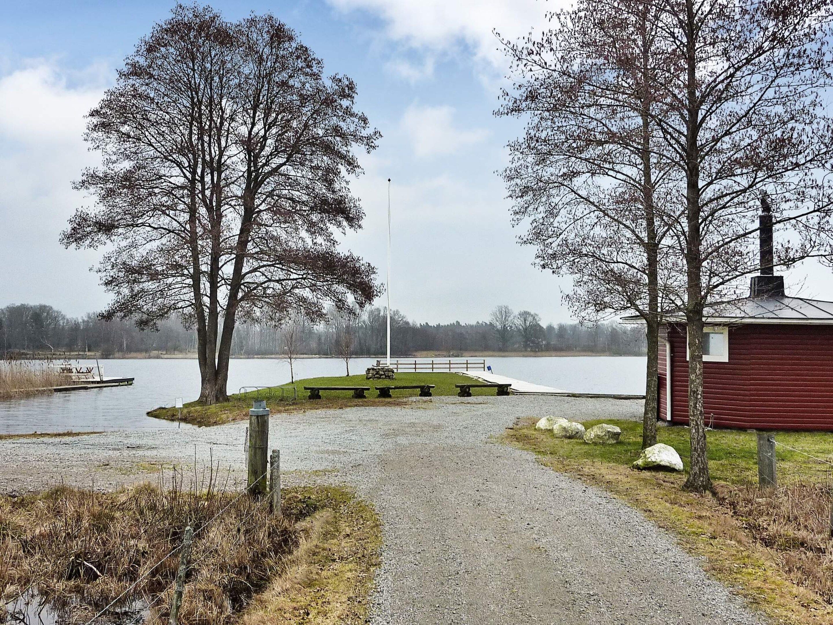 A gravel path leading to a dock by a lake, surrounded by trees and a small red building.
