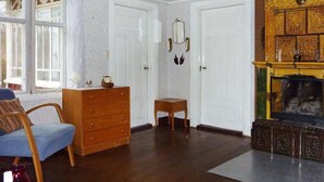 A room with a wooden dresser, a blue chair, a small table, and a fireplace with ornate decorations. - 5 Person Holiday Home in Kalvsvik (Kalvsvik)