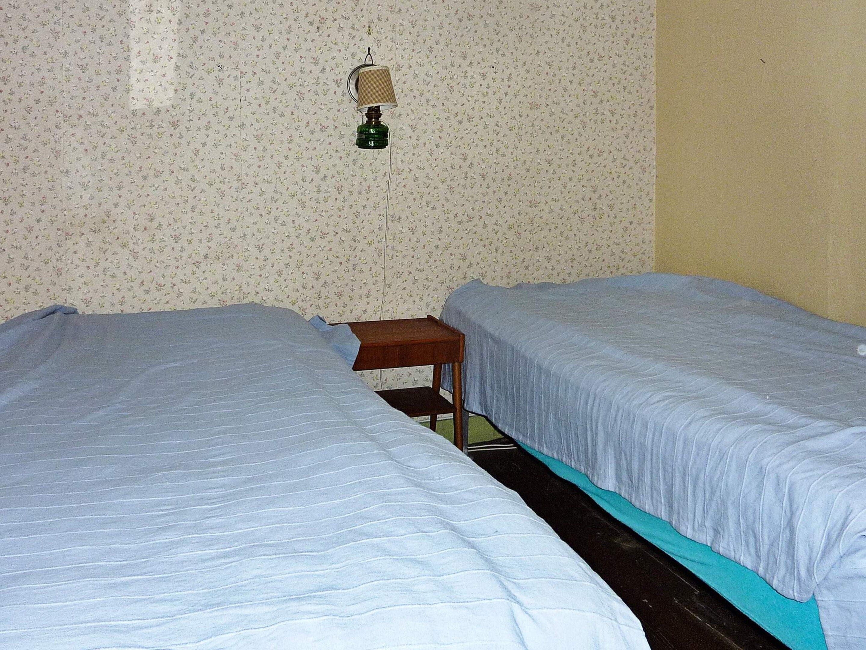 A room with two beds, a small wooden table, and a wall-mounted lamp.