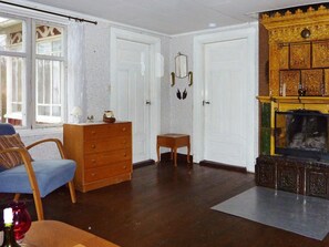 A room with a wooden dresser, a blue chair, a small table, and a fireplace with intricate carvings. - 5 Person Holiday Home in Kalvsvik (Kalvsvik)