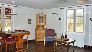 A dining area with a wooden table and chairs, a cabinet with glassware, and a window with curtains. - 5 Person Holiday Home in Kalvsvik (Kalvsvik)
