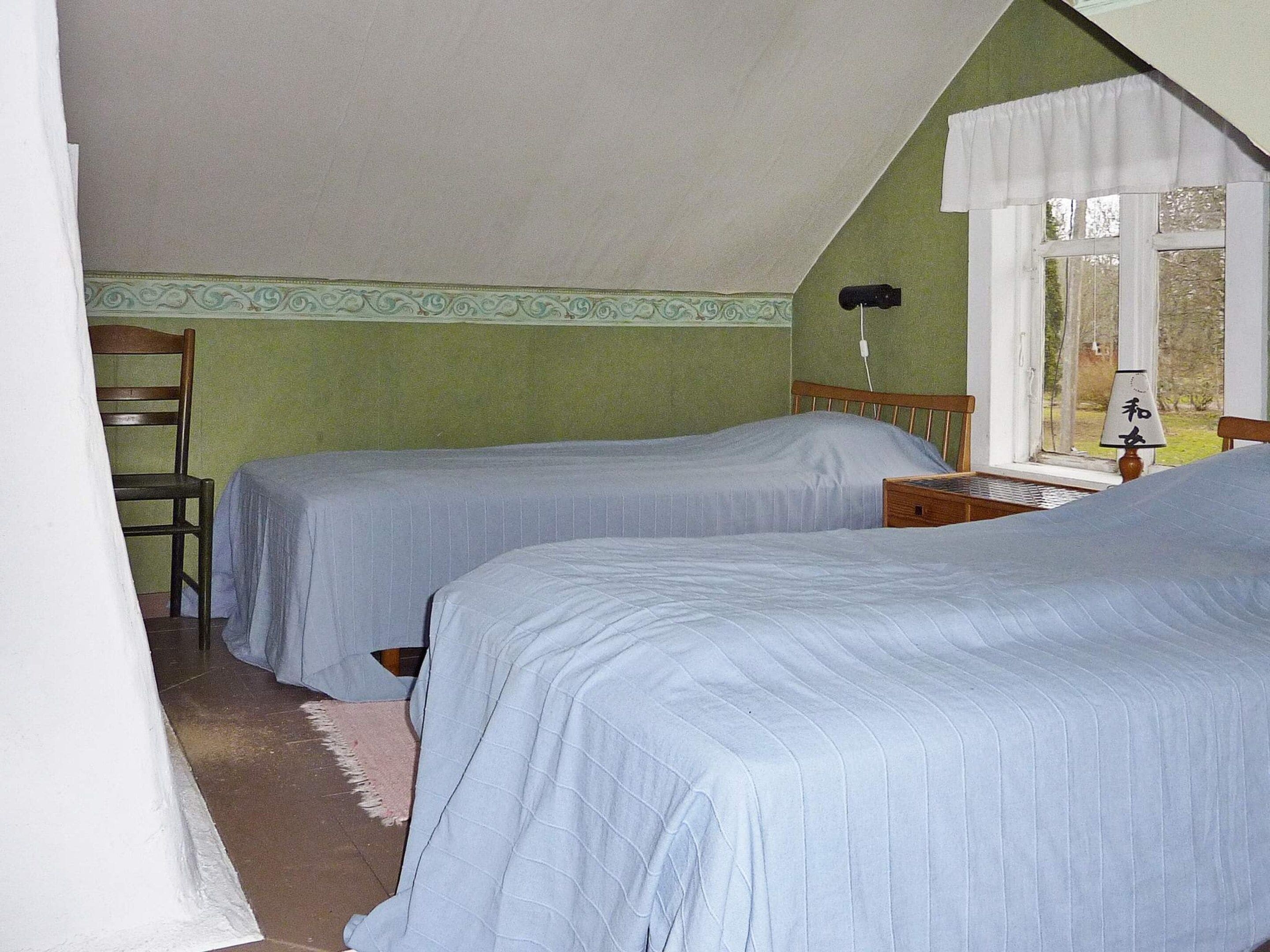 Habitación con dos camas, una silla, una ventana con cortinas y una lámpara en una mesita de noche.