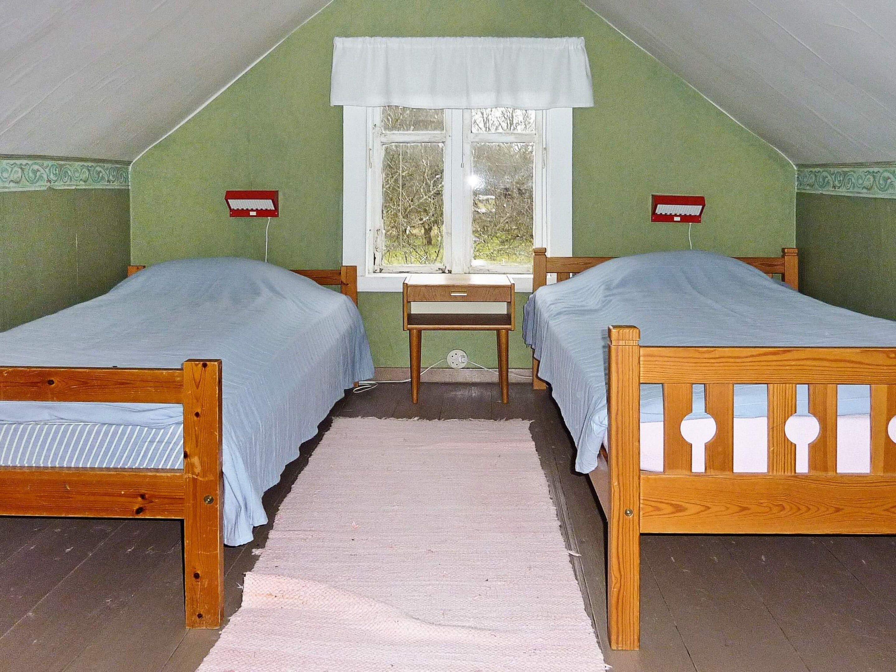 A room with two wooden beds, a small desk, and a window with a white valance.