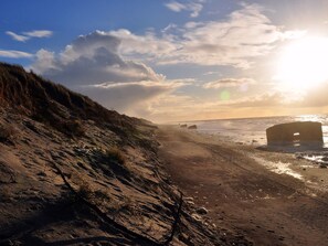 A beach with a clear sky, a sandy path, and a large rock formation in the water.