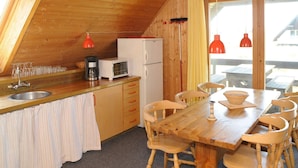 A wooden interior with a kitchen, dining table, chairs, and a refrigerator.