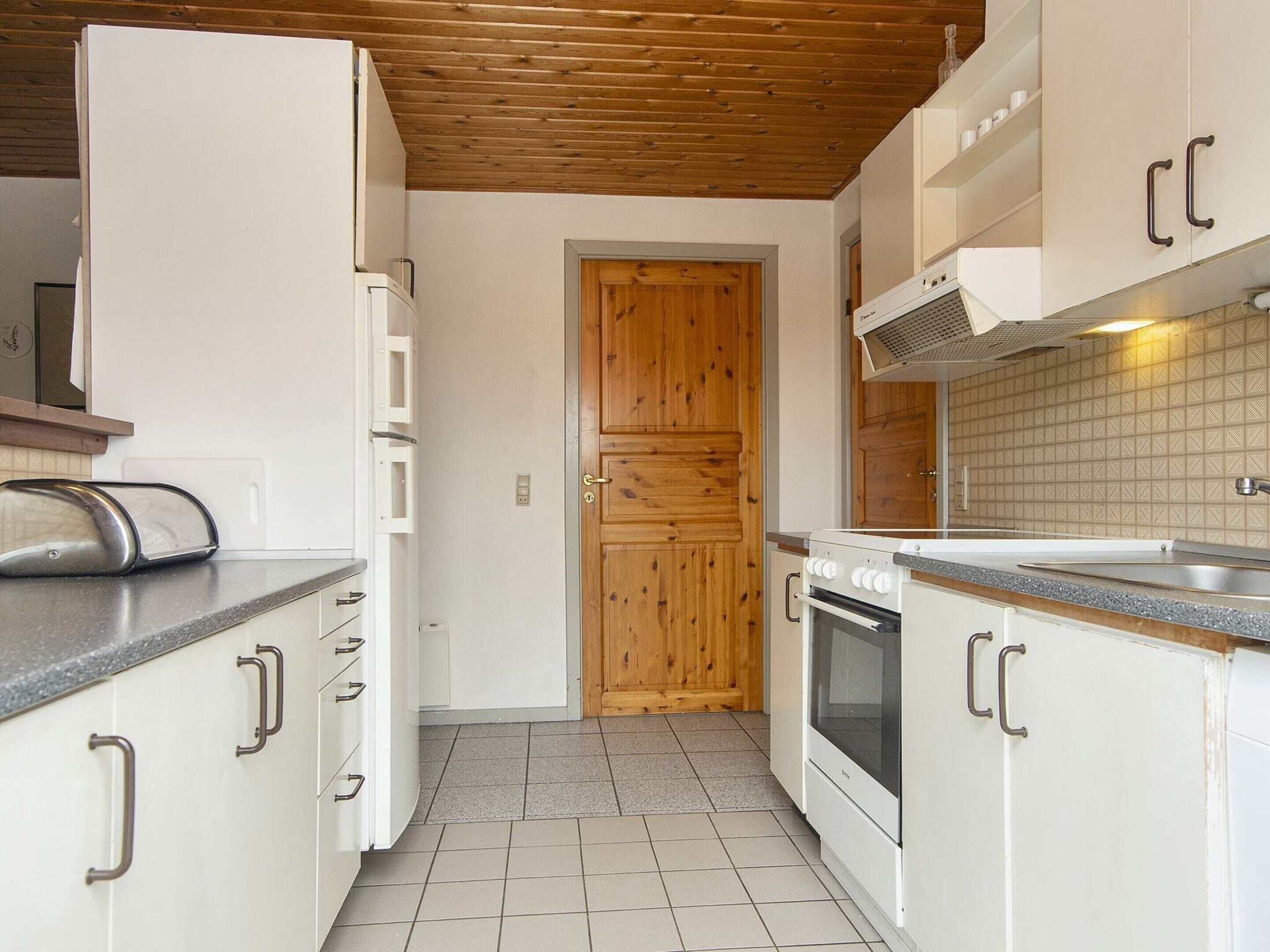 A compact kitchen with white cabinets, a wooden door, and a tiled floor.