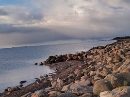Una costa rocosa con grandes rocas y piedras, que desemboca en aguas tranquilas.