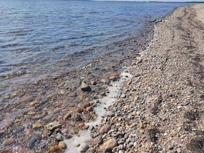 Una playa de guijarros con agua cristalina y una costa lejana.