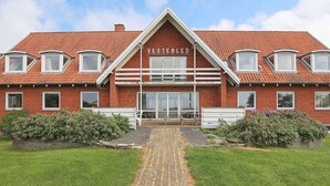 A red-brick building with the name 'VESTERLED' on the facade, featuring a central entrance with glass doors, surrounded by a paved pathway and greenery.