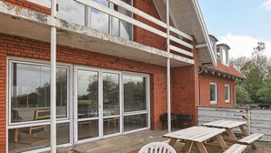 A brick building with large windows and a covered patio area with wooden tables and chairs.