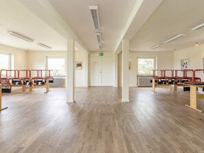 A spacious room with wooden flooring, multiple seating areas with red chairs, and a white door with an exit sign. - 40 Person Holiday Home in Hurup Thy (Hurup Thy)