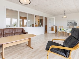 Una sala moderna con un sofá, una mesa de comedor y una silla. Se ve un área de cocina a través de una puerta de vidrio.