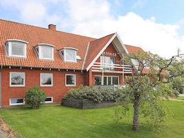Et rødt murhus med skråt tag, mange vinduer og en velplejet græsplæne.
