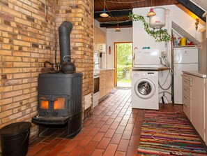 A kitchen with a brick wall, a wood-burning stove, a washing machine, and a refrigerator. - 2 Person Holiday Home in Ejstrupholm (Ejstrupholm)