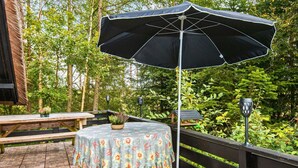 Un patio con una mesa cubierta por un mantel floral, un paraguas negro y una maceta verde.