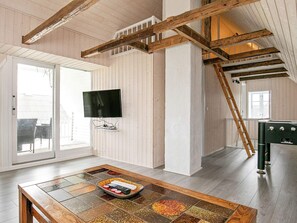 A spacious room with a wooden ceiling, a television mounted on the wall, a dining table with a remote control, and a ladder in the corner. - 4 Star Holiday Home in Vestervig (Vestervig)
