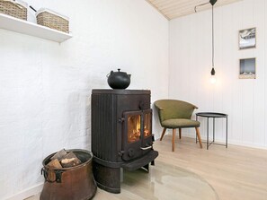 A room with a wood-burning stove, a chair, a small table, and a hanging light fixture. - 4 Star Holiday Home in Vestervig (Vestervig)