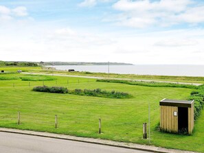 A grassy field with a small wooden structure, a road, and a body of water in the distance.