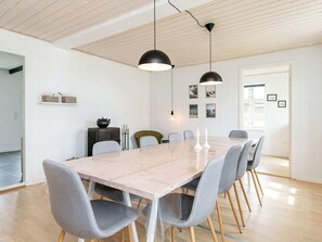 A modern dining room with a marble table, grey upholstered chairs, black pendant lights, and framed pictures on the wall.