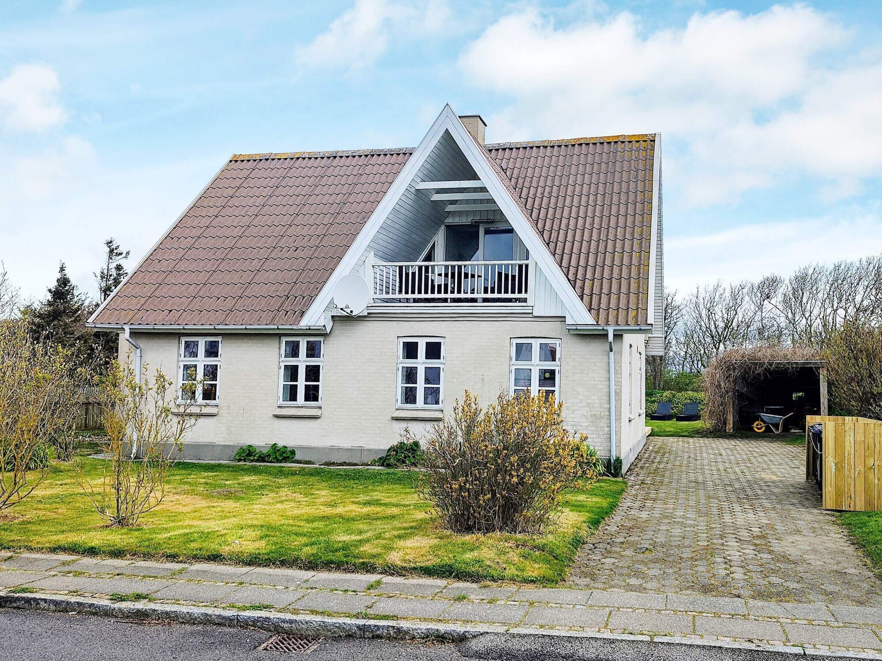 A two-story house with a sloped roof, a balcony, and a driveway leading to a garage.