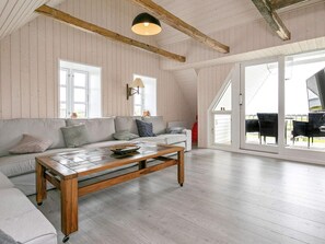 A spacious living room with a wooden coffee table, a sofa, and a large sliding glass door leading to an outdoor area. - 4 Star Holiday Home in Vestervig (Vestervig)