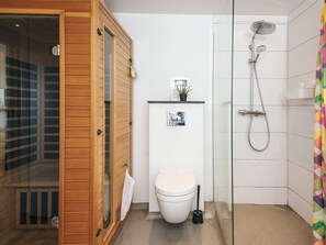 Ein modernes Badezimmer mit einer Holztür zur Sauna, einer Toilette, einer Dusche und einem kleinen Regal mit einer Pflanze.