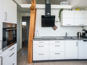 Eine moderne Küche mit weißen Schränken, einem eingebauten Backofen, einer schwarzen Dunstabzugshaube und einer Wand in Holzoptik.