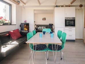 Ein modernes Wohnzimmer mit Kamin, einem Esstisch mit Stühlen, einer Couch und einer Küchenzeile mit Schränken und Geräten.