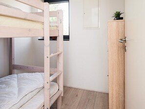A bunk bed with a wooden ladder, a wooden wardrobe, and a window with a view of greenery.