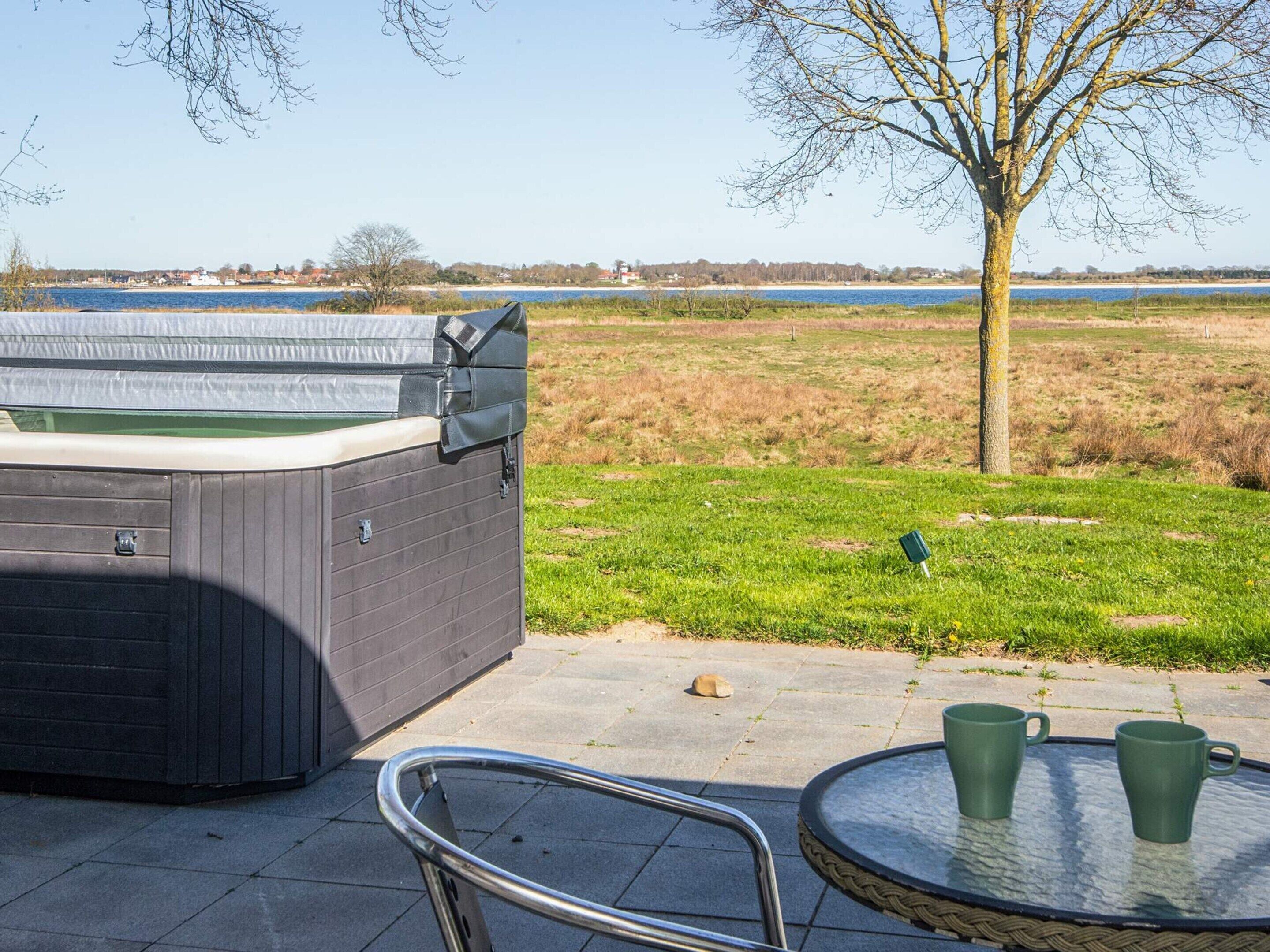 Un jacuzzi en un área con césped, con vista a un cuerpo de agua y un árbol.
