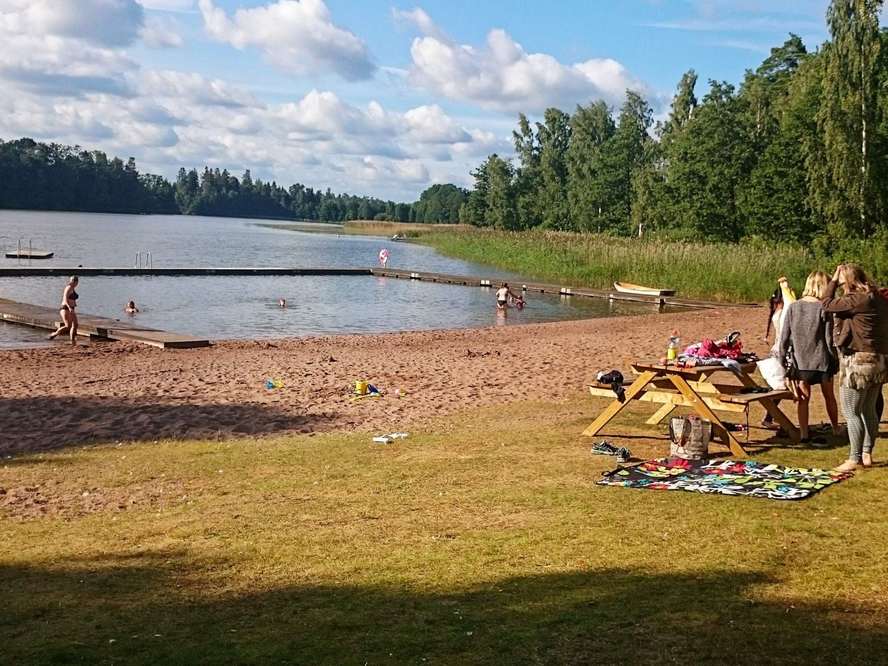 A lakeside setting with a sandy beach, a dock, and picnic tables.