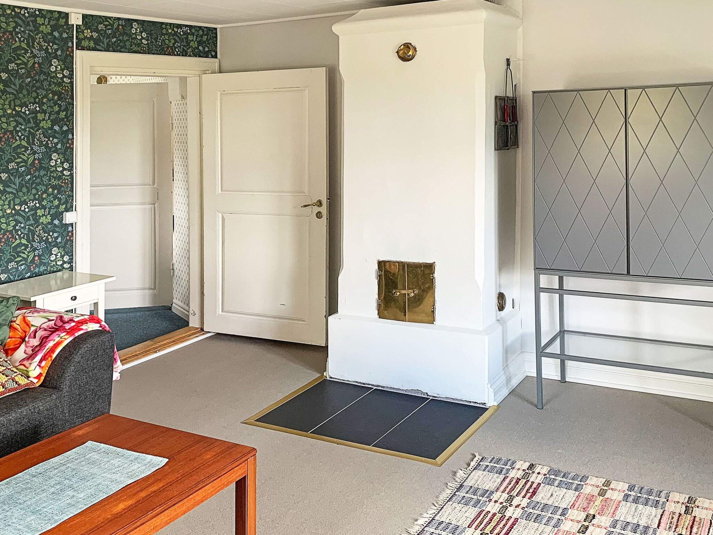 A room with a sofa, a wooden table, a patterned rug, a white cabinet with a diamond-patterned door, and a door with a brass handle.