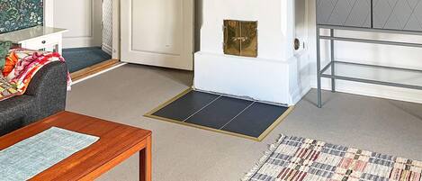 A room with a sofa, a wooden table, a patterned rug, a white cabinet with a diamond-patterned door, and a door with a brass handle.