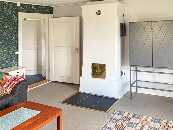 A room with a sofa, a wooden table, a patterned rug, a white cabinet with a diamond-patterned door, and a door with a brass handle. - Holiday Home in Gedser (Gamleby)