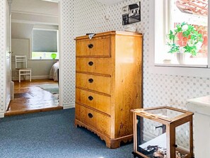 A room with a wooden dresser, a framed picture on the wall, and a window with a plant. - Holiday Home in Gedser (Gamleby)