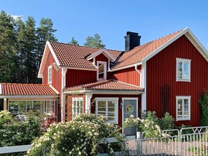 Ein rotes Holzhaus mit einem Ziegeldach, weißem Zierrat und einem kleinen Garten mit weißen Blumen.