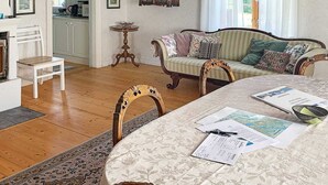 A cozy living room with a sofa, chairs, a dining table with papers, a cabinet, and a view of the kitchen. - Holiday Home in Gedser (Gamleby)