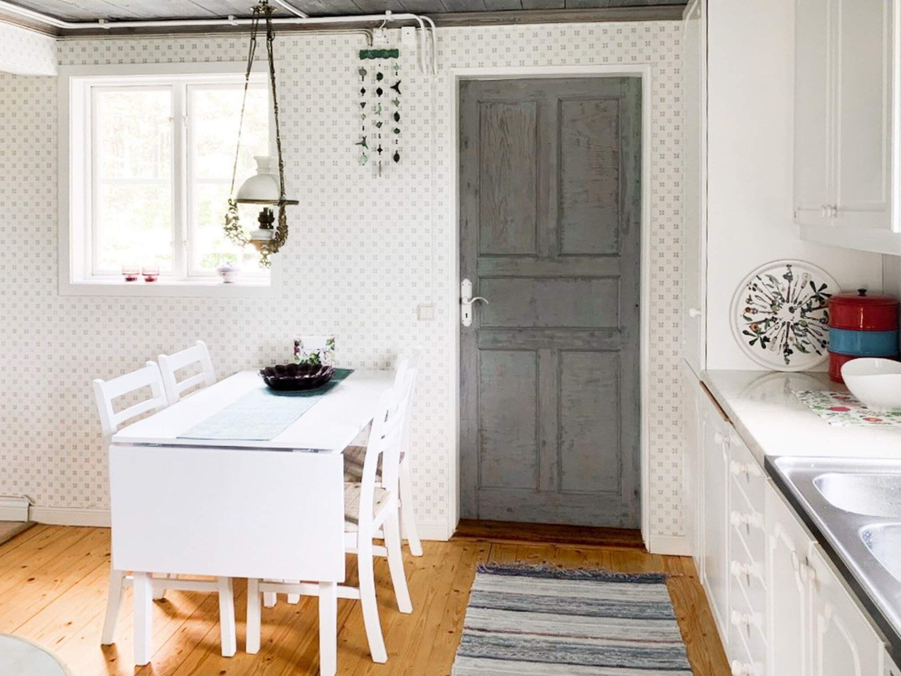 A kitchen with a white table, chairs, a wooden door, and a window with a hanging light fixture.