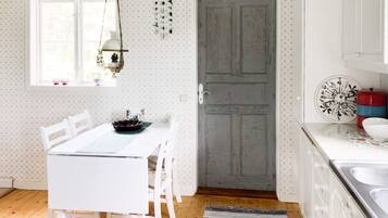 A kitchen with a white table, chairs, a wooden door, and a window with a hanging light fixture.