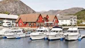 A red building with a sign reading "KRO" and "PAB," docked boats, and a mountainous backdrop. - 10 Person Holiday Home in Bygstad (Sunnfjord)