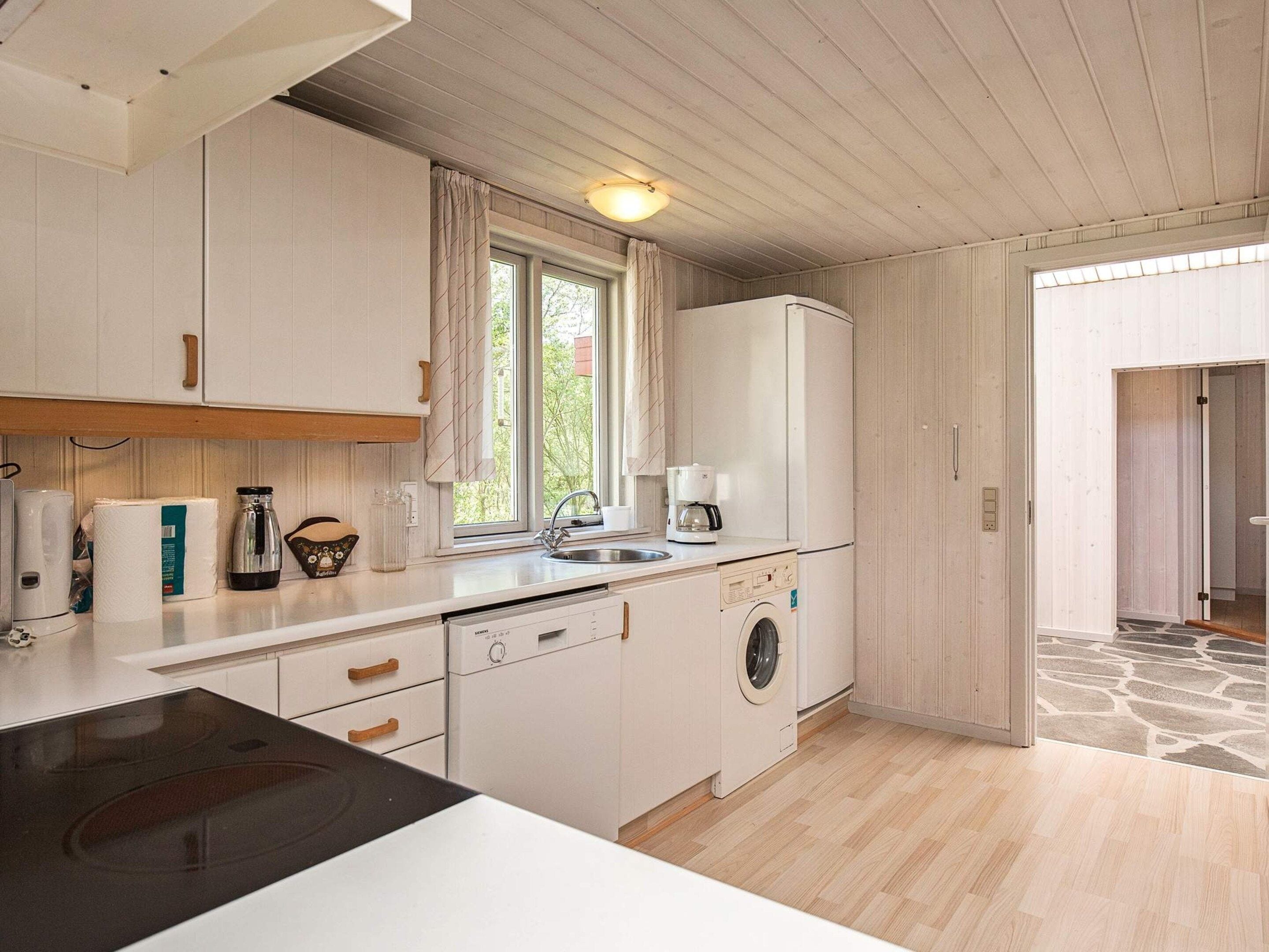 A compact kitchen with white cabinets, a built-in dishwasher, a coffee maker, and a washing machine.