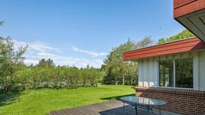 Une terrasse dotée d’une table et de chaises à plateau en verre, d’un mur en briques et offrant une vue sur une cour verdoyante avec des arbres.