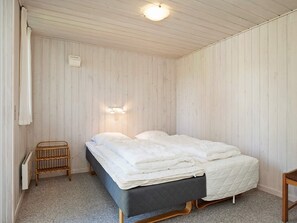 Un lit simple avec une tête de lit sombre, dans une pièce aux murs recouverts de panneaux de bois et au design simple et fonctionnel.