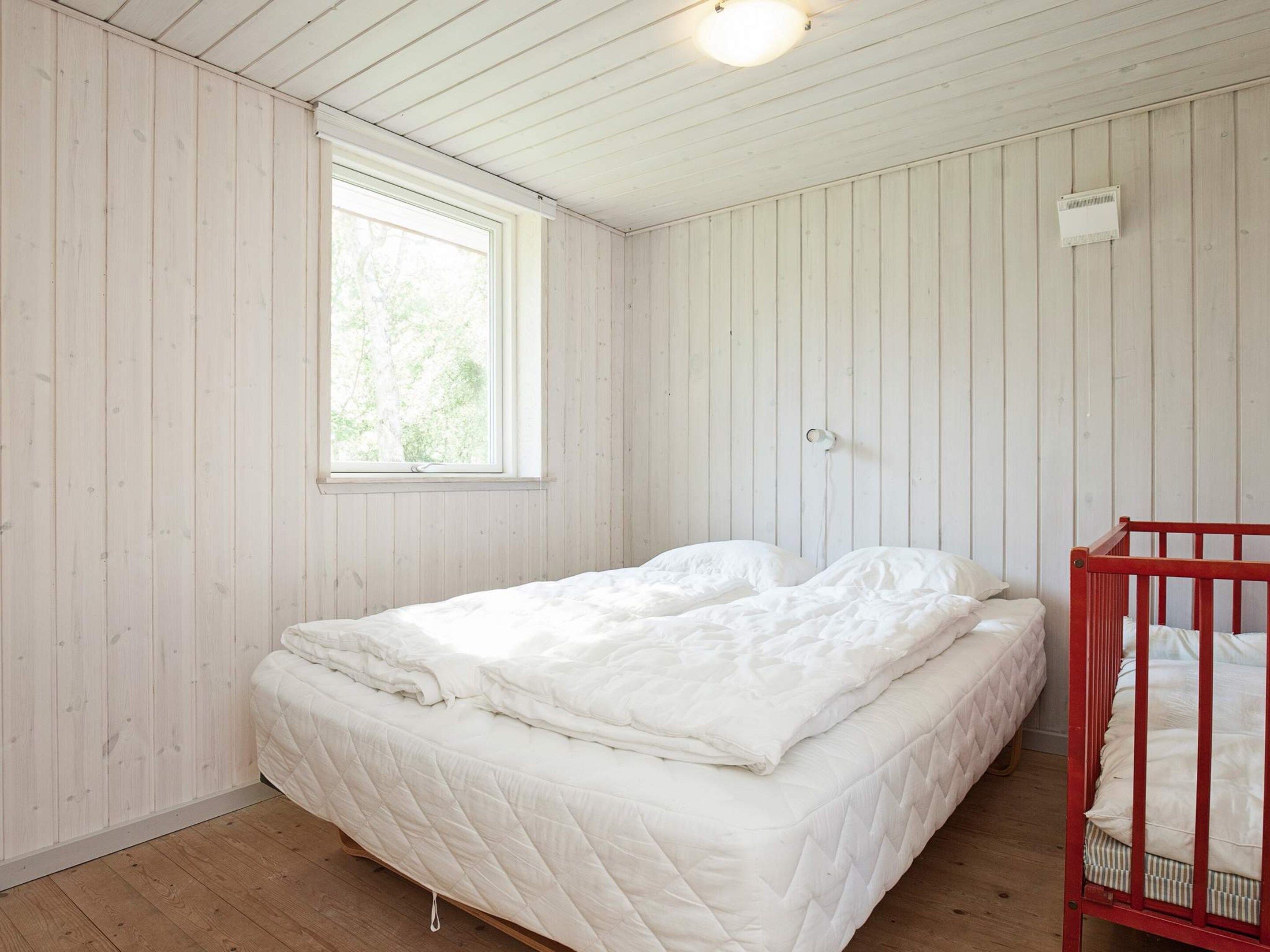 A room with a bed, a crib, a window, and wooden walls.