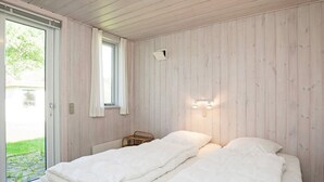 Une chambre avec deux lits, une fenêtre avec des rideaux, un luminaire fixé au mur et une petite table.