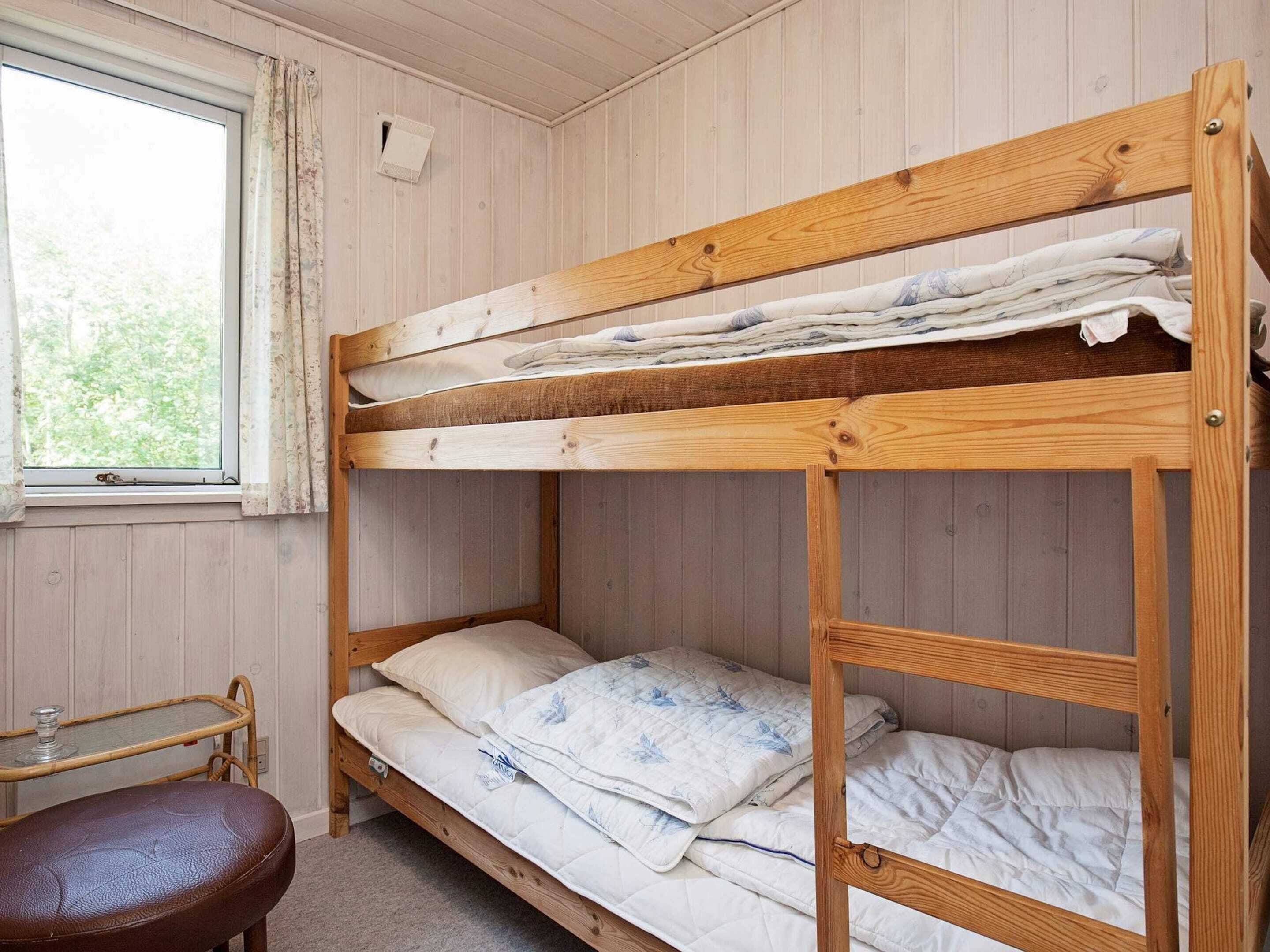 A bunk bed room with a window, a small table, and a bench.