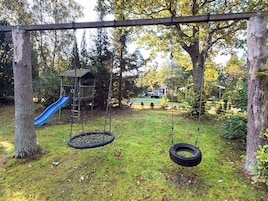 A playground with a swing set and tire swings, surrounded by trees and a grassy area.